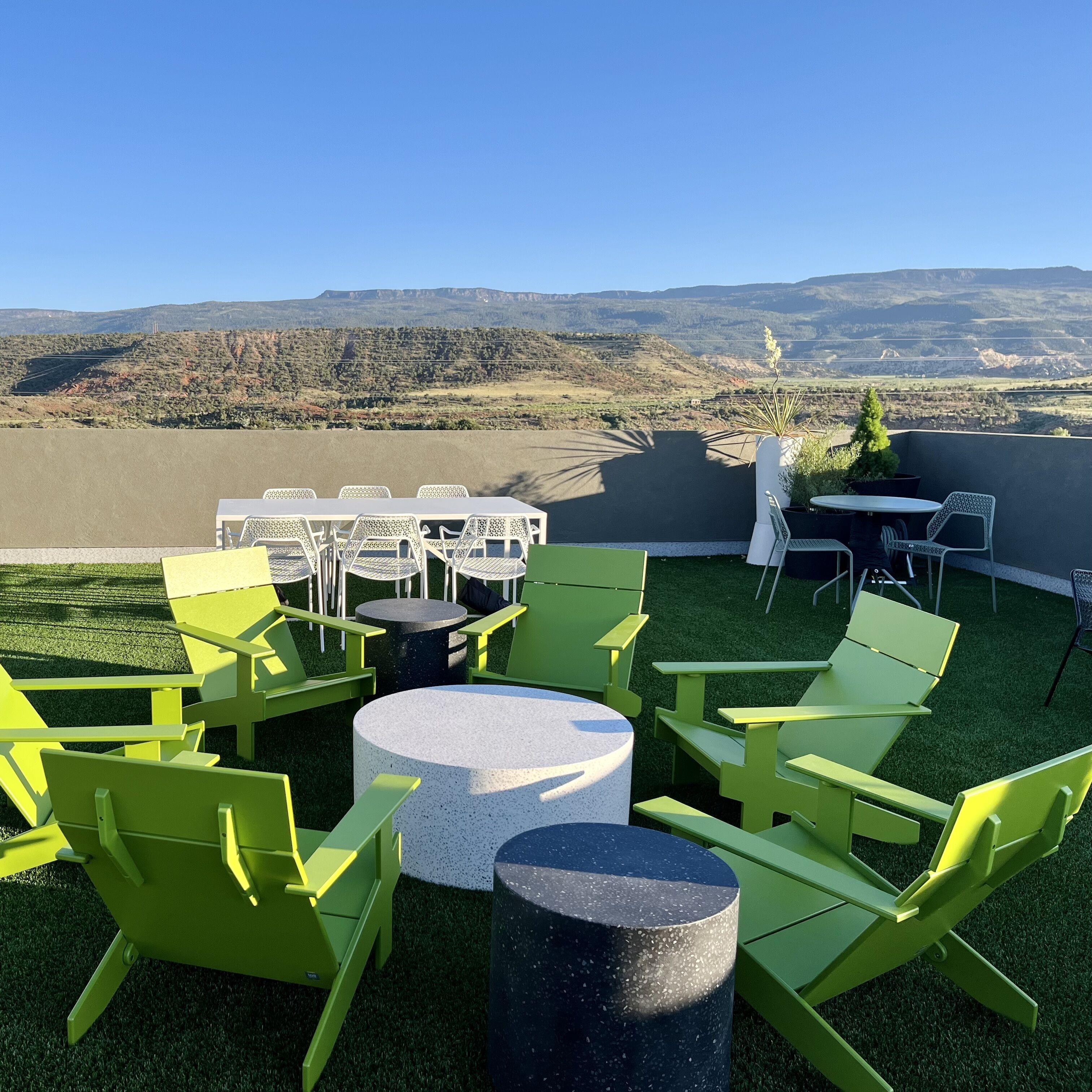 A rooftop terrace with green chairs and tables, offering a view of distant mountains.