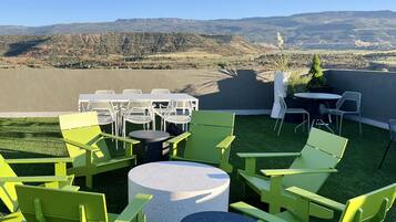 A rooftop terrace with green chairs and tables, offering a view of distant mountains.