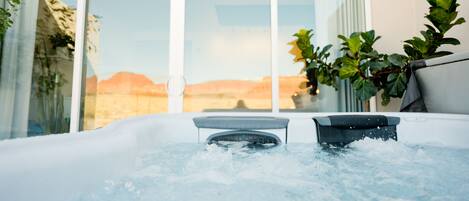 Un jacuzzi con vistas a un paisaje desértico a través de amplios ventanales correderas.