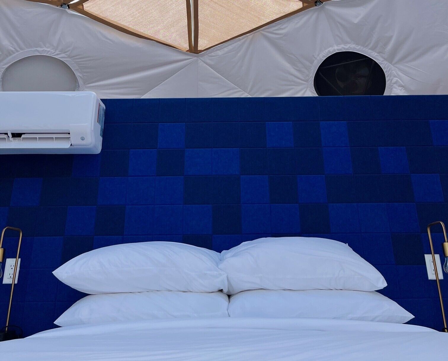Een bed met witte beddengoed, een blauw hoofdeinde en een airconditioner bevestigd aan de muur.