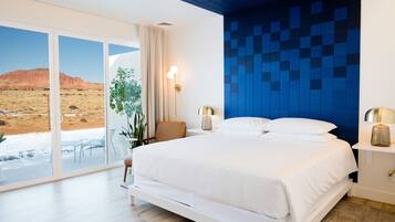 Un dormitorio moderno con una cama grande, vista a un paisaje desértico a través de puertas corredizas de vidrio y una pared decorativa con azulejos azules.