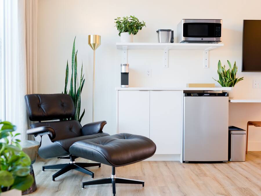 A modern living room with a leather sofa, a dining area with a microwave, and a TV on the wall.