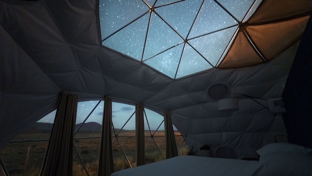 A tented accommodation with a bed, a view of the stars through a geometric window, and a landscape outside. - Skyview Hotel (Torrey)