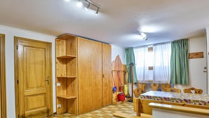 A room with a wooden wardrobe, a bed with a floral bedspread, a checkered floor, and a window with green curtains. - Residence Cervinia ID 522 (Valtournenche)
