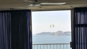 Una habitación con vista al mar, un balcón con barandilla, una mesa con sillas y un ventilador de techo.