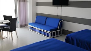 Habitación de hotel con dos camas, un sofá, un televisor montado en la pared y una zona de comedor con mesa y sillas.