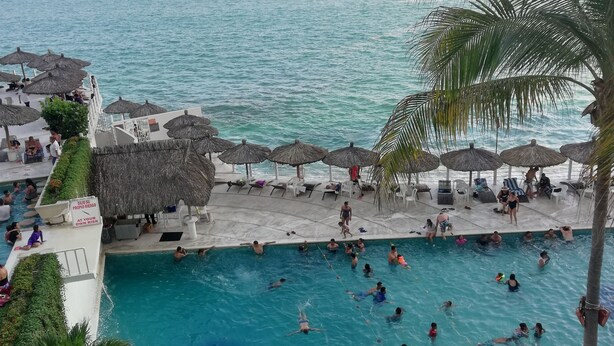 Zona de piscina con múltiples sombrillas y sillas de descanso, rodeada de una vista panorámica del mar.