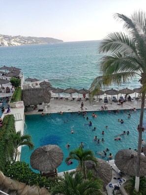 A pool area with multiple umbrellas and lounge chairs, surrounded by a scenic view of the sea. - Spectacular Twin Towers Suite (Acapulco)