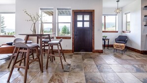 Amplia habitación con comedor que incluye una mesa y sillas, ventanas grandes con vistas y una puerta de madera oscura.