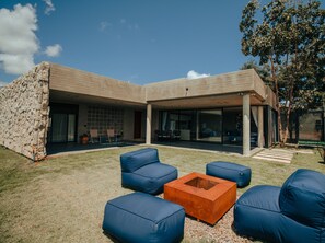 A modern house with a stone exterior, a covered patio area with blue outdoor furniture, and a fire pit. - Casa Upanjí + Pool + Breakfast Option (Alto Paraíso de Goiás)