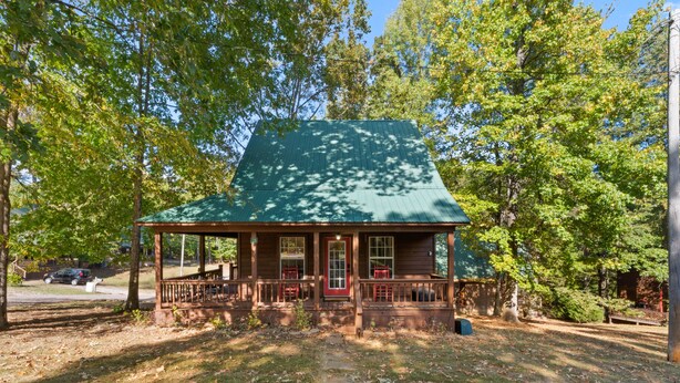 A wooden cabin with a green roof, a porch with red railings, and a front door.