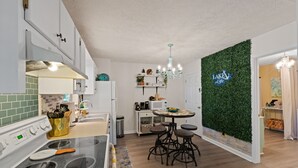 A modern kitchen with white cabinets, a stove, and a dining area with stools.
