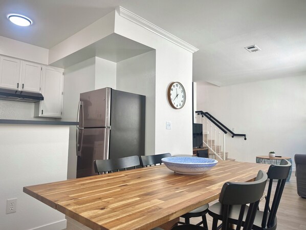 A modern kitchen with white cabinets, a stainless steel refrigerator, a wooden dining table with chairs, a blue ceramic bowl, and a wall clock. - Your Private Oasis in the Hub of Marina del Rey (Marina del Rey)