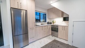 A modern kitchen with light wood cabinets, stainless steel appliances, and a large window providing natural light. - Chic CBD Townhouse | Walk to One NZ Stadium & SALT (Christchurch)