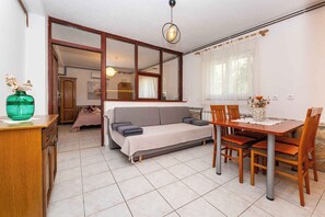Un espacio habitable compacto con sofá, mesa de comedor y sillas, un armario de madera y un gran ventanal con cortinas.