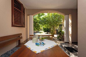 Un pasillo con un banco de madera, una mesa con un mantel individual, una jarrón de vidrio y un cuenco de fruta.