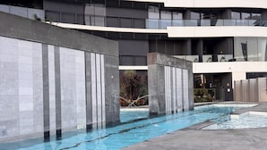 Um edifício moderno com área de piscina, apresentando fachada curva, amplas janelas e piso revestido.