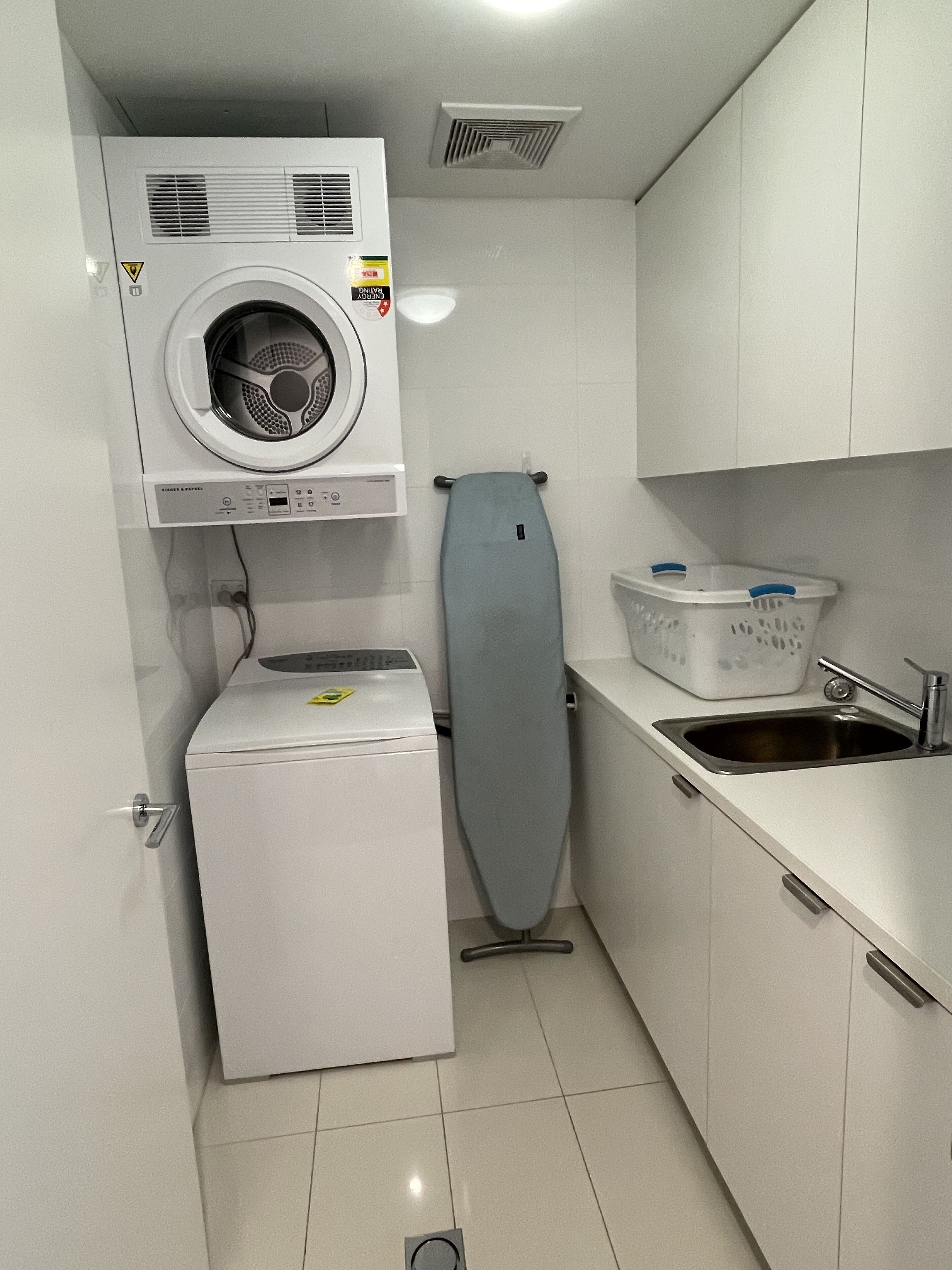 A compact laundry area with a washing machine, dryer, ironing board, and a sink.