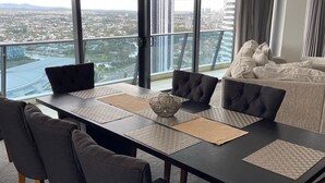 Uma sala de jantar moderna com uma mesa grande, cadeiras escuras e vista para a paisagem urbana através de amplas janelas.