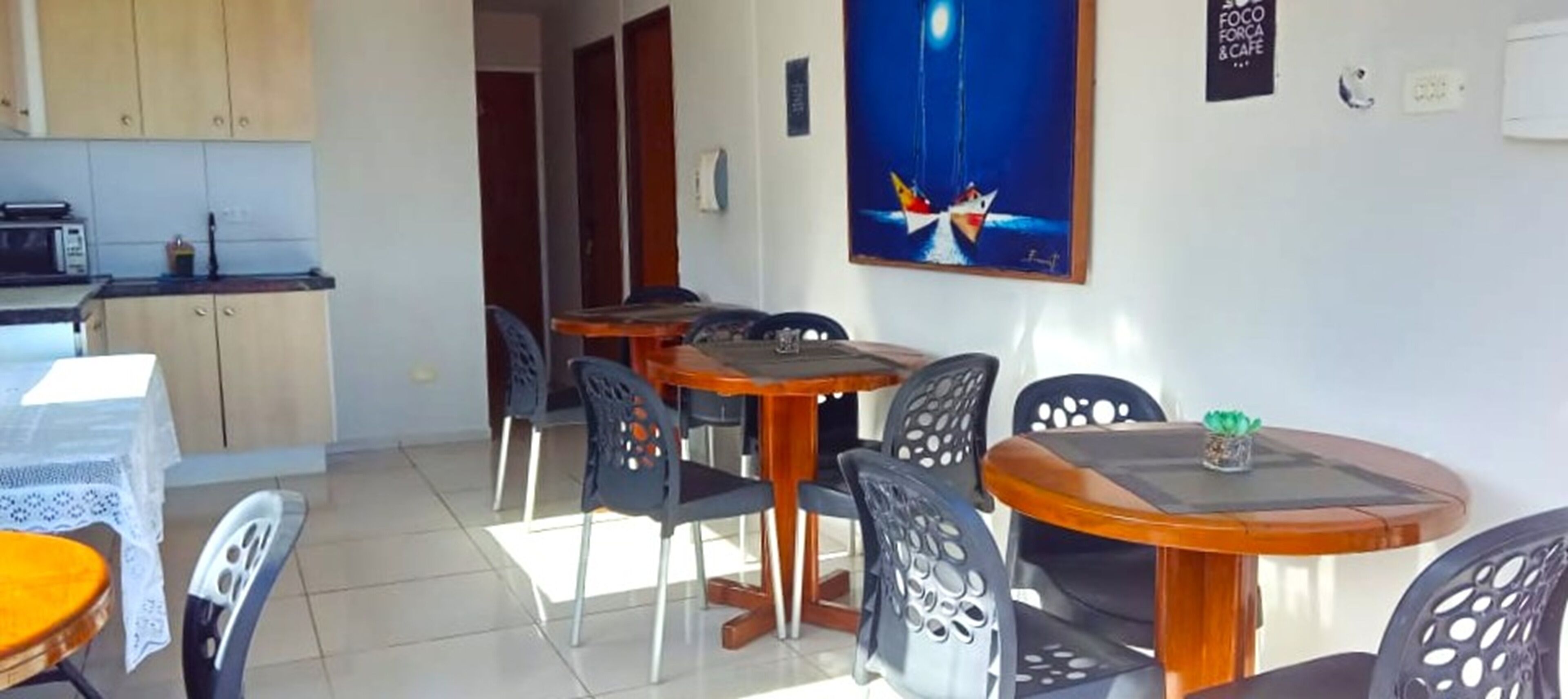 Un comedor con mesas y sillas redondas, una cocina al fondo y un cuadro en la pared.