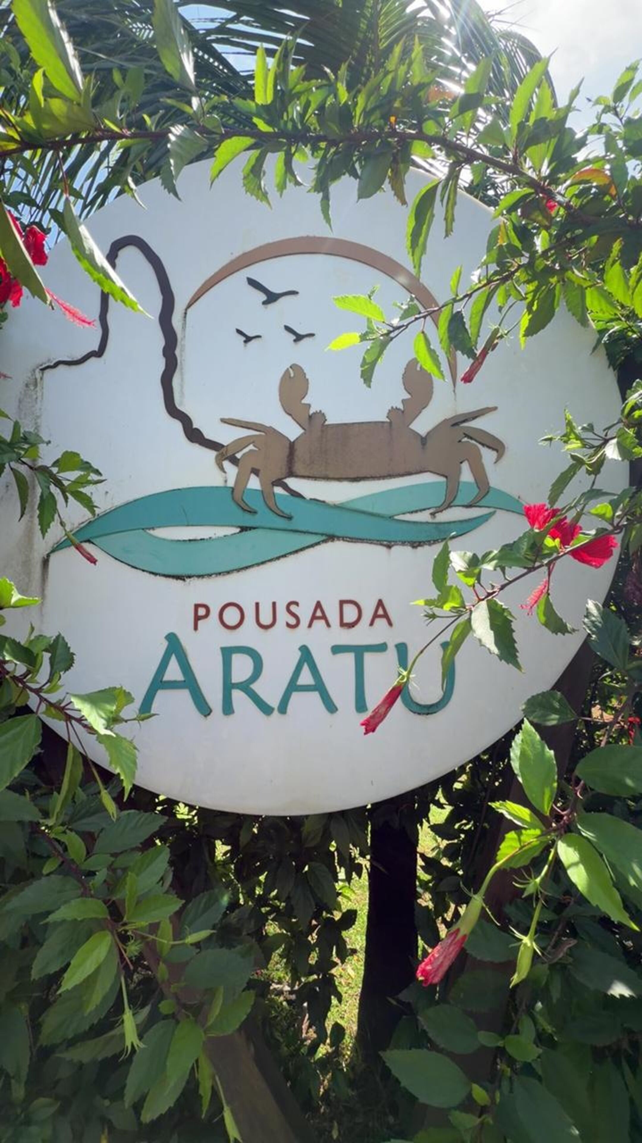 A circular sign with a silhouette of a person on a boat, surrounded by greenery and red flowers.