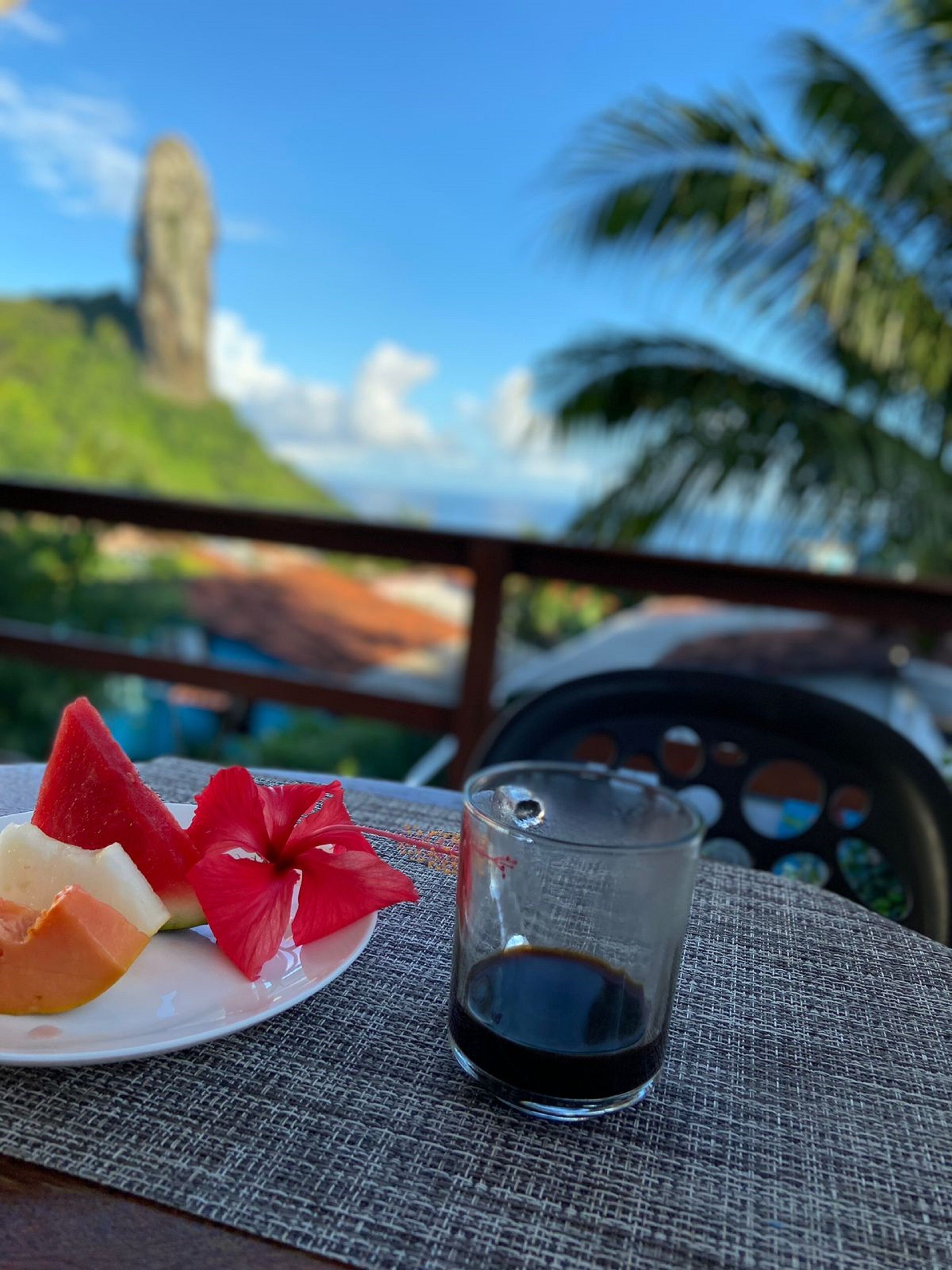 Ein Teller mit Obst und ein Glas dunkler Flüssigkeit, vermutlich Kaffee, auf einer strukturierten Tischdecke.