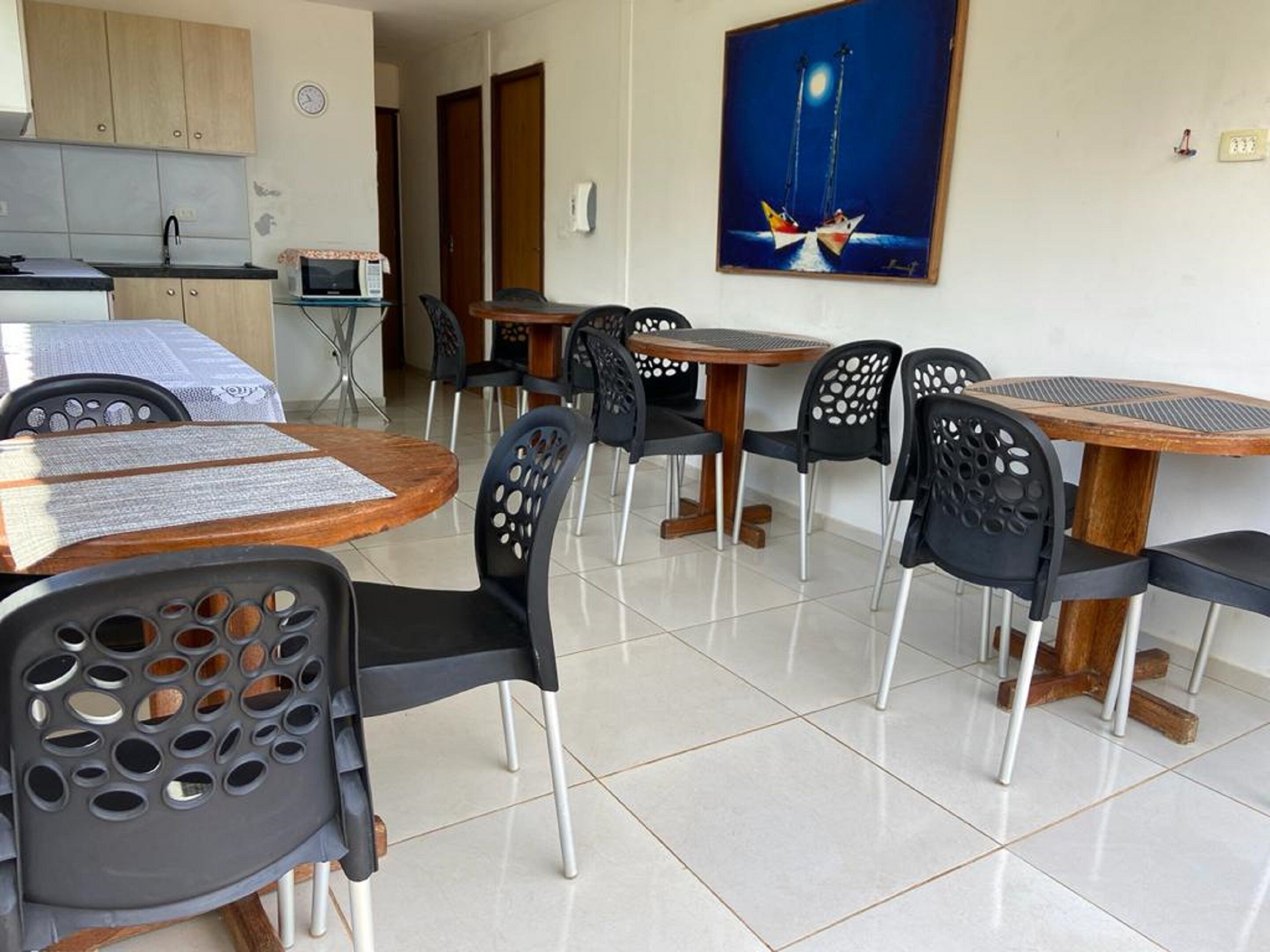 Un comedor con mesas y sillas redondas, una cocina al fondo y un cuadro en la pared.