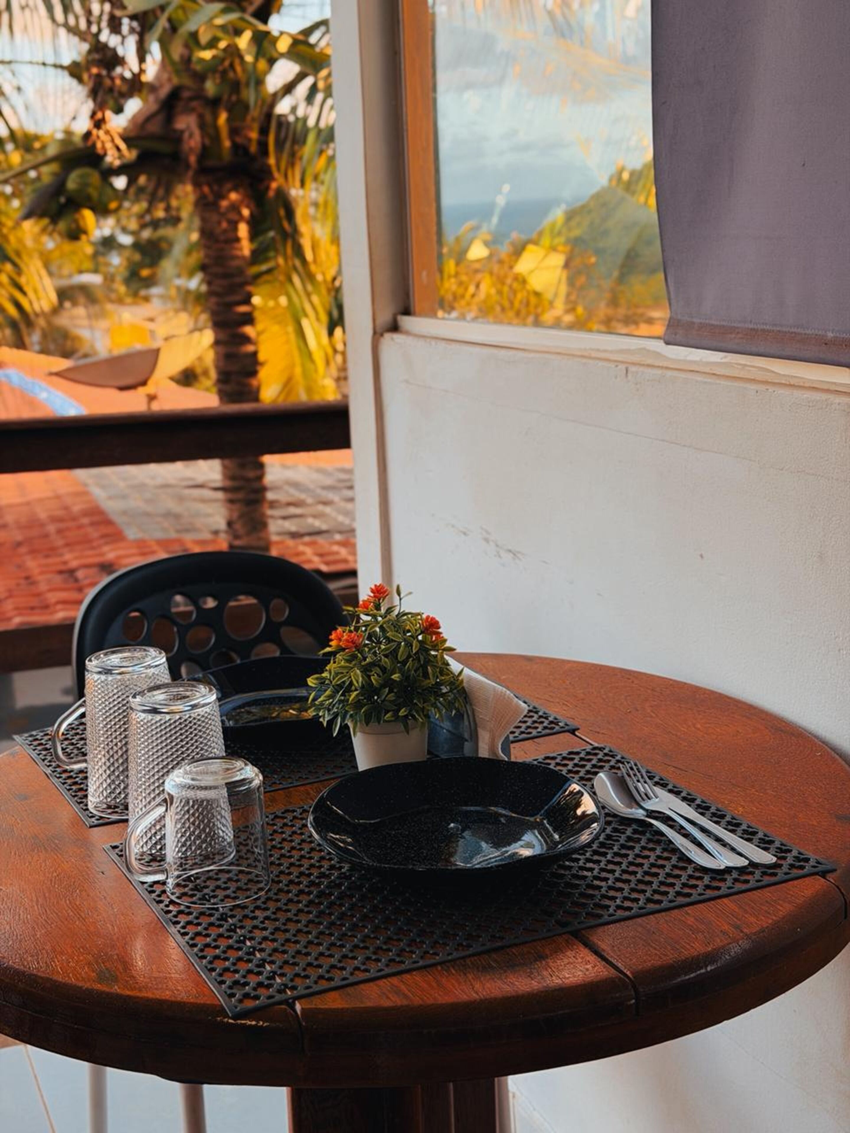 Uma mesa de madeira redonda com um jogo americano preto, uma pequena planta em vaso e uma tigela preta.
