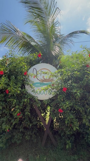 Un letrero con una palmera y flores rojas, rodeado de follaje.