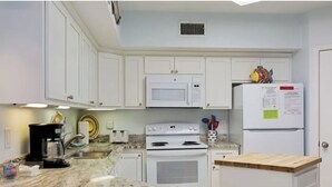 A kitchen with white cabinets, a microwave, a stove, a refrigerator, and a wooden countertop. - Beautiful Beach Views! Discounts for longer stays in November-March (Orange Beach)