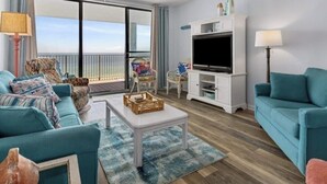 A living room with a sofa, a coffee table, a TV, and a balcony with a view. - Beautiful Beach Views! Discounts for longer stays in November-March (Orange Beach)