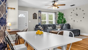 A dining area with a white table and chairs, a bowl of fruit, and a ceiling fan.