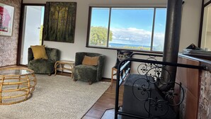Een ruime woonkamer met een groot raam met uitzicht op zee, twee groene fauteuils, een klein bijzettafeltje en een decoratieve metalen balustrade.