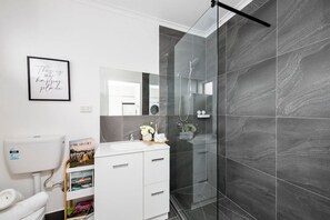 A modern bathroom with a glass shower enclosure, a white sink, and a framed quote on the wall. - Sun and Sand Albert Park (Albert Park)