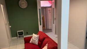 A red sofa with a white pillow in a room with green walls, white ceiling, and tiled floor.