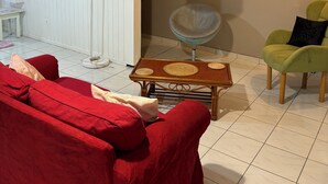 A room with a red sofa, a wooden coffee table, a green armchair, a woven basket, and a staircase with wooden railings.