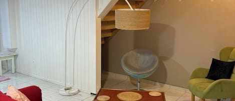 Una habitación con un sofá rojo, una mesa de centro de madera, un sillón verde, una cesta tejida y una escalera con barandillas de madera.