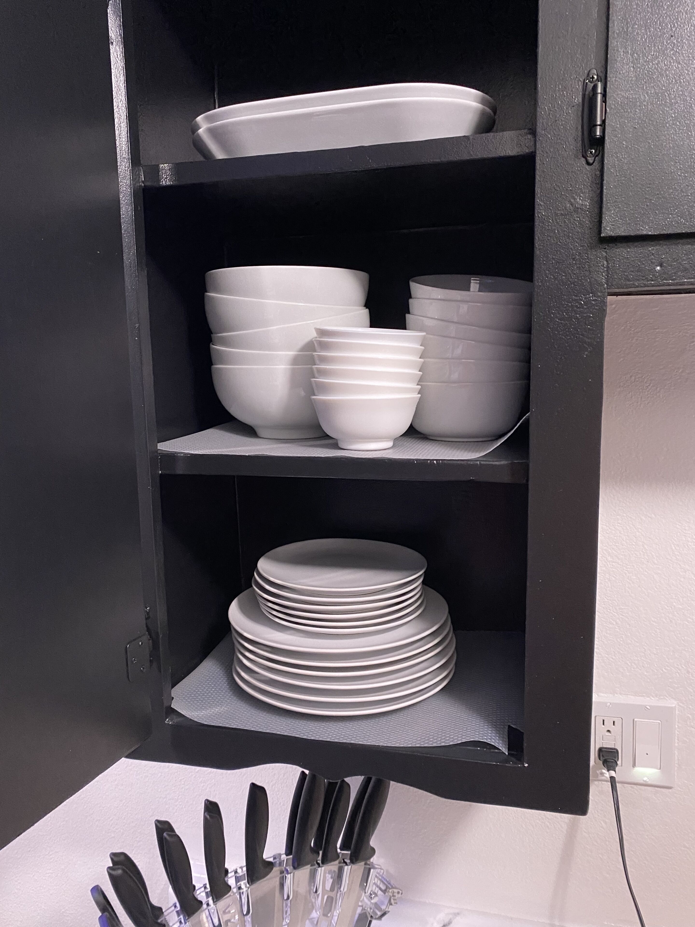 A kitchen cabinet with shelves holding white dishes and plates.