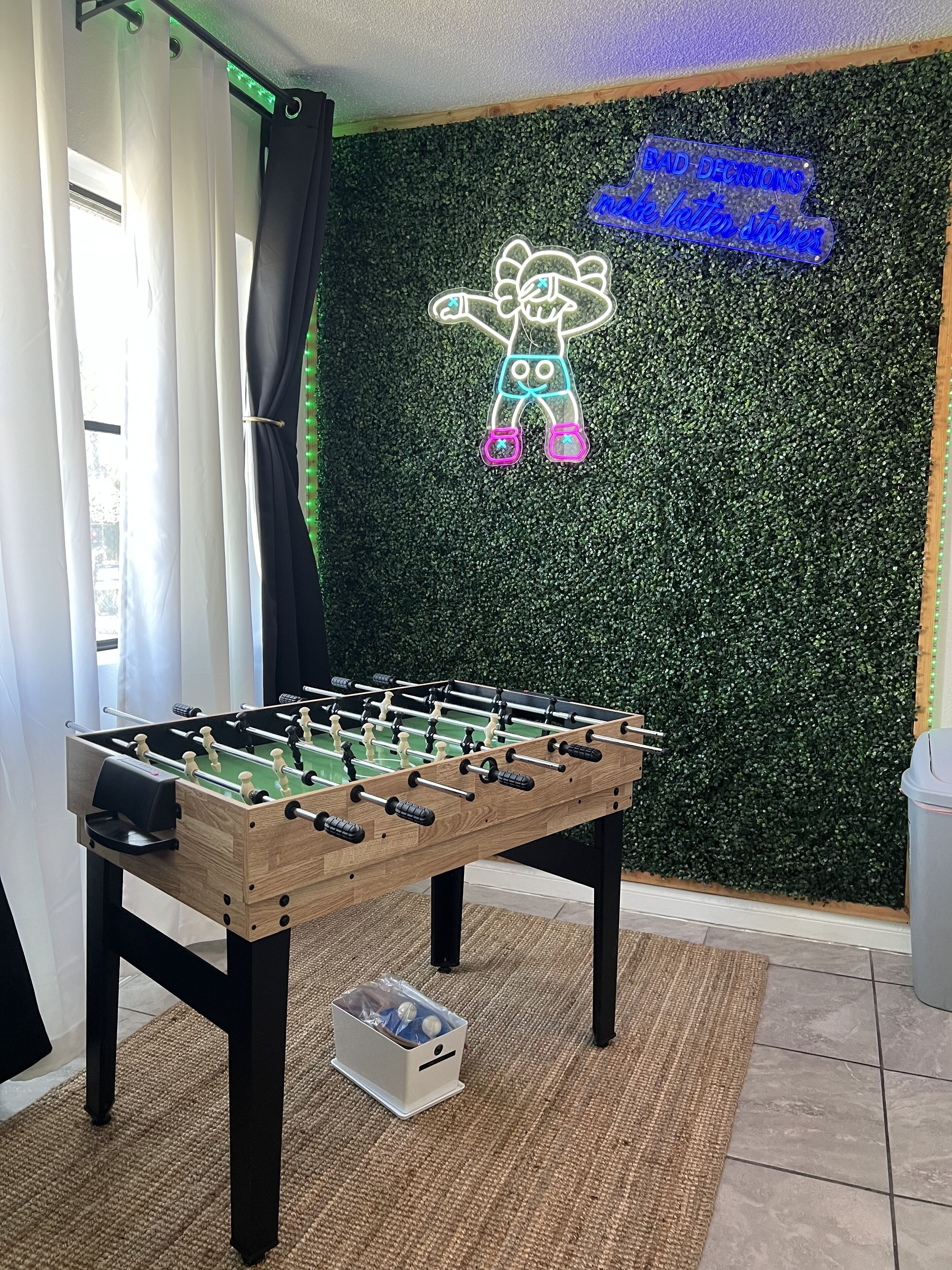 A foosball table in a room with a green wall and a neon sign.