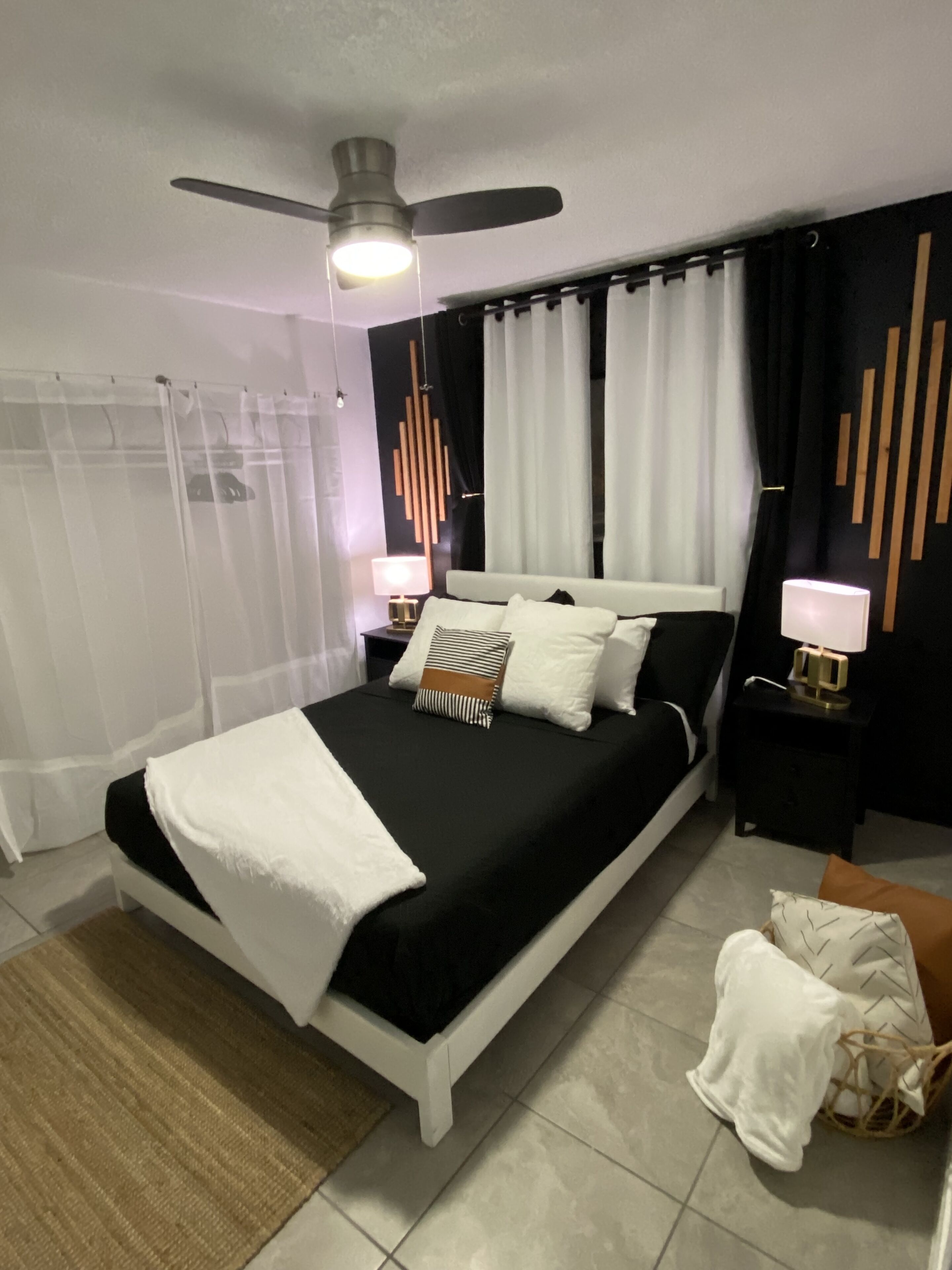 Une chambre à coucher moderne, avec un lit, un ventilateur de plafond, une table de chevet avec une lampe et un panneau décoratif mural.