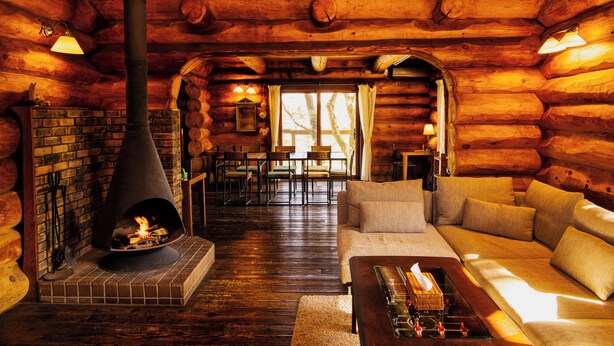 Ein rustikaler Innenraum einer Blockhütte mit Kamin, Holzwänden, einer Couch und einem Essbereich.