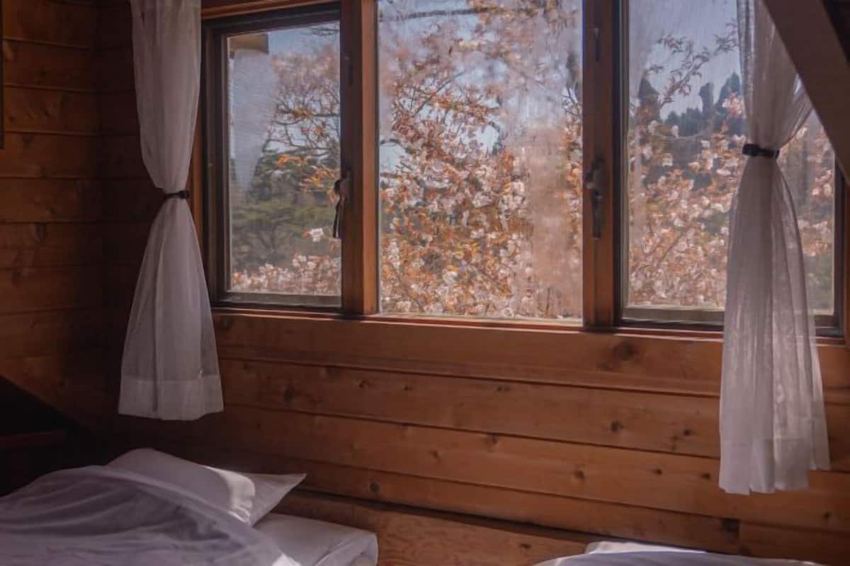 Two beds with crisp white bedding, set against a backdrop of trees with vibrant autumn foliage.