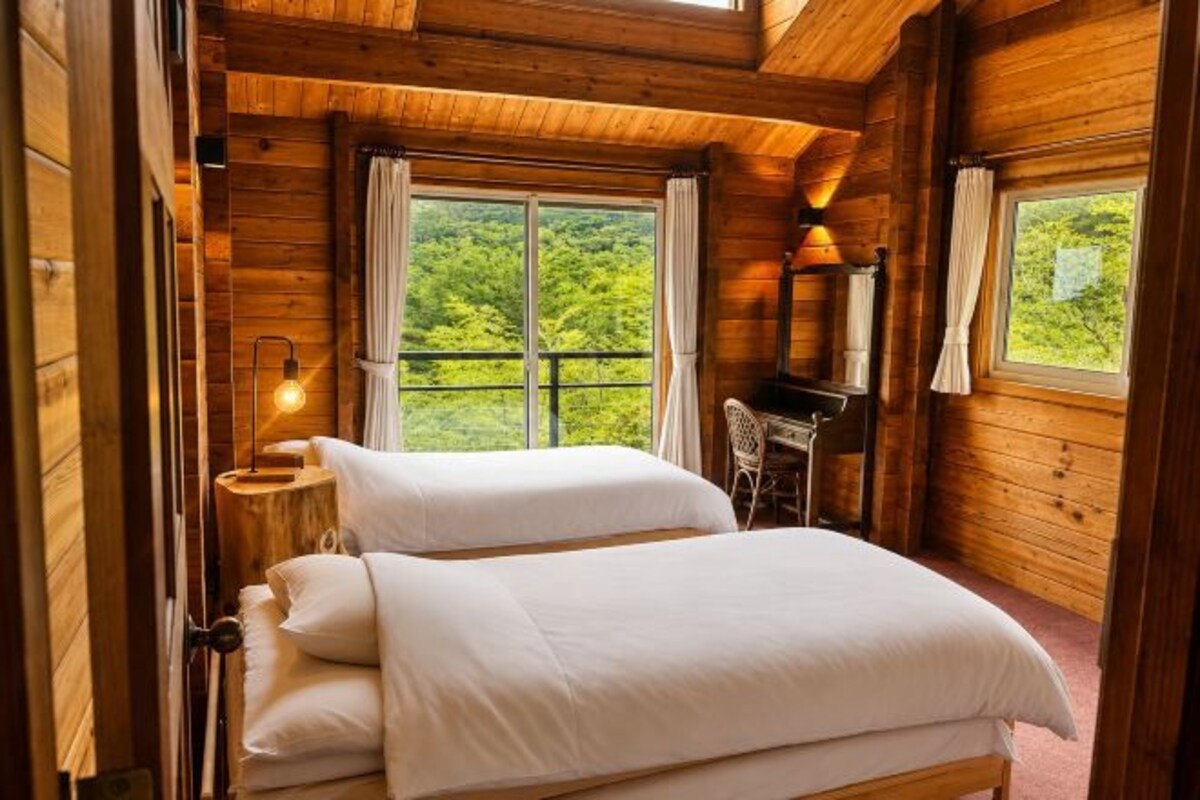 A wooden cabin bedroom with a bed, a desk, and a window with curtains.