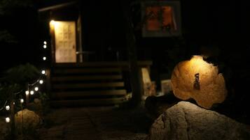 A nighttime scene with a pathway leading to a building, illuminated by string lights and a single spotlight on a rock.