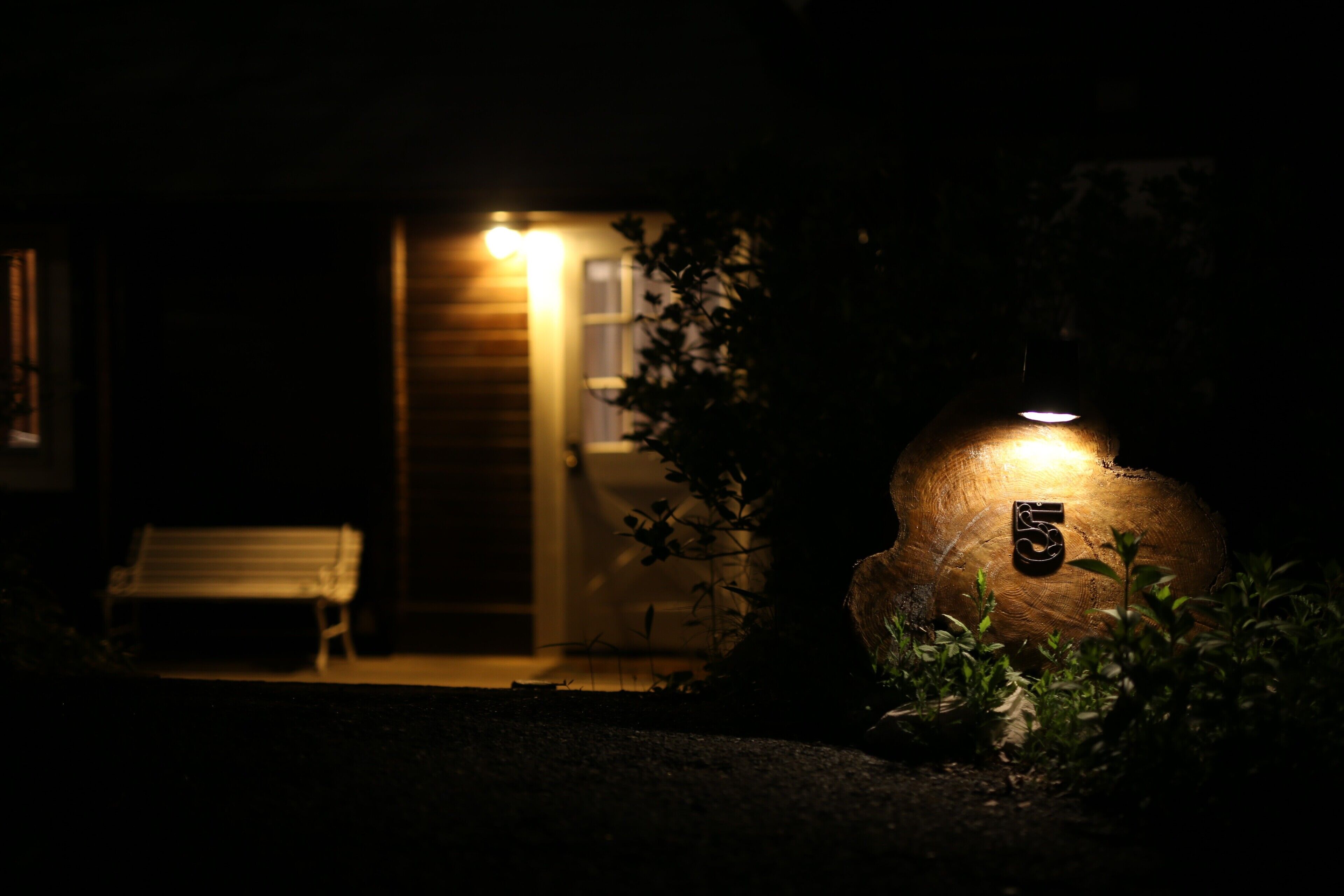 A dimly lit outdoor area with a bench and a wooden structure with a light.