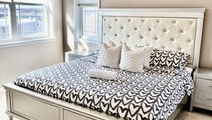 A bedroom with a large bed, a nightstand, and a window with blinds. - Charming 3BR & 2.5Ba nested in KOP w free parking, close to Conshy & Philly. (Bridgeport)