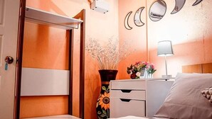 A bedroom with a bed, a nightstand, a dresser, a mirror, and a wall-mounted shelf.