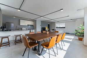 Una cucina moderna con mobili bianchi, un'isola centrale e un'area pranzo con tavolo in legno e sedie arancioni.