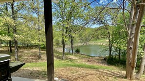 A patio area with a grill, overlooking a lake surrounded by trees. - Cozy and Relaxing Lake House close to Lake of the Arbuckles (Sulphur)