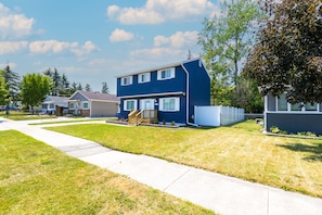 A two-story residential house with a front yard, a sidewalk, and a fence. - Pet-Friendly | Large Group | Hot Tub - All Year (Bay City)
